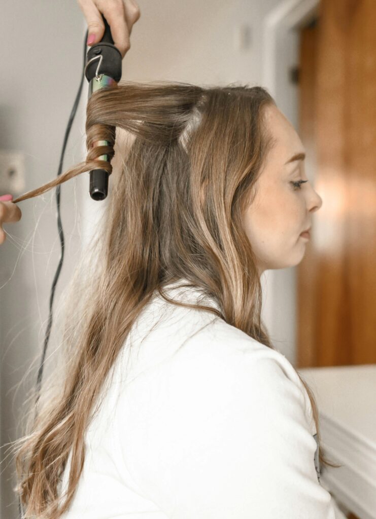 Profile of a woman having her hair curled with an iron in a salon setting| makeup studio